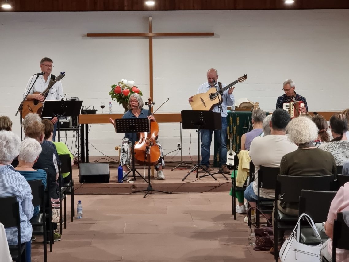 Benefizkonzert für das Hospiz Sophia - "Übers Meer - Von Meerbusen und Seesäcken" Musiker spielen live in einer Kirche vor einem Publikum. Kreuz im Hintergrund sichtbar.