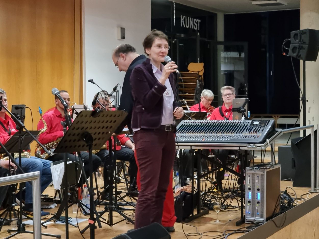 Benefizkonzert der Rhein-Nahe Big Band Dr. Maresa Biesterfeld spricht am Mikrofon vor der Rhein-Nahe Big Band.