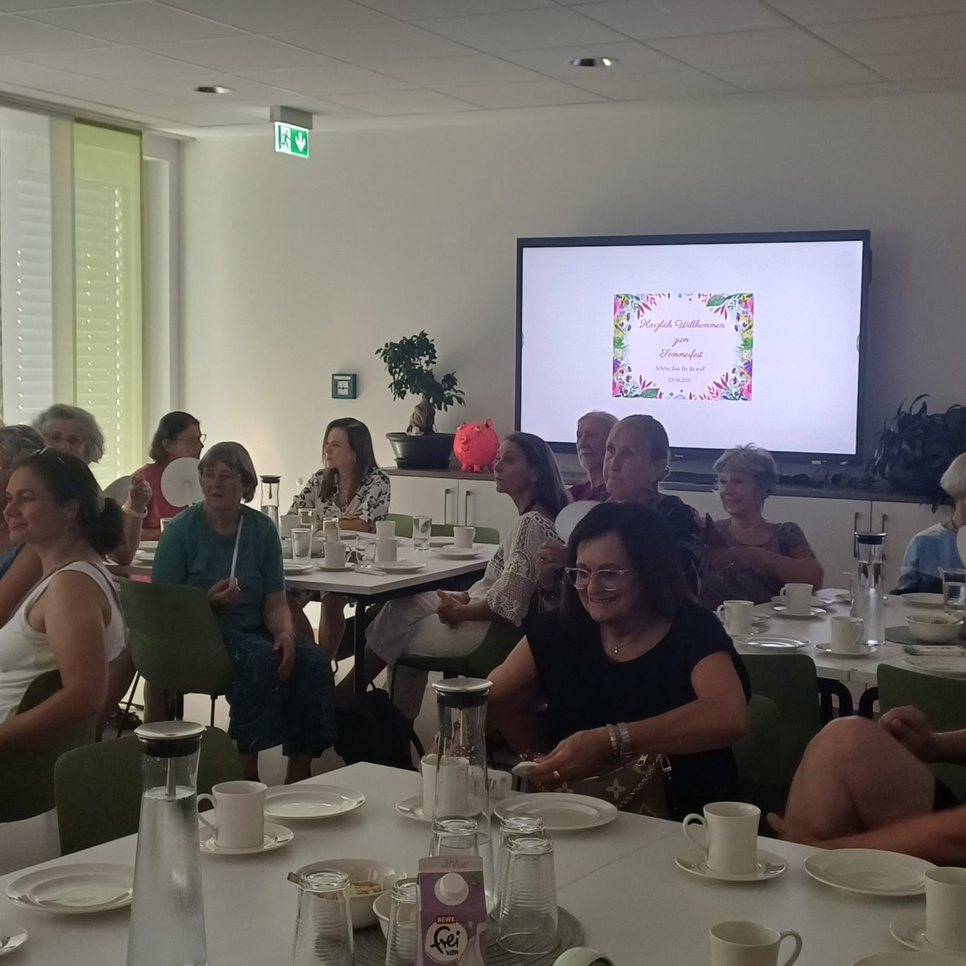 23. Juni 2026 Sommerfest für unsere ehrenamtlichen Helferinnen und Helfer Eine Gruppe von Personen sitzt an einem Tisch in einem hellen Raum und unterhält sich.