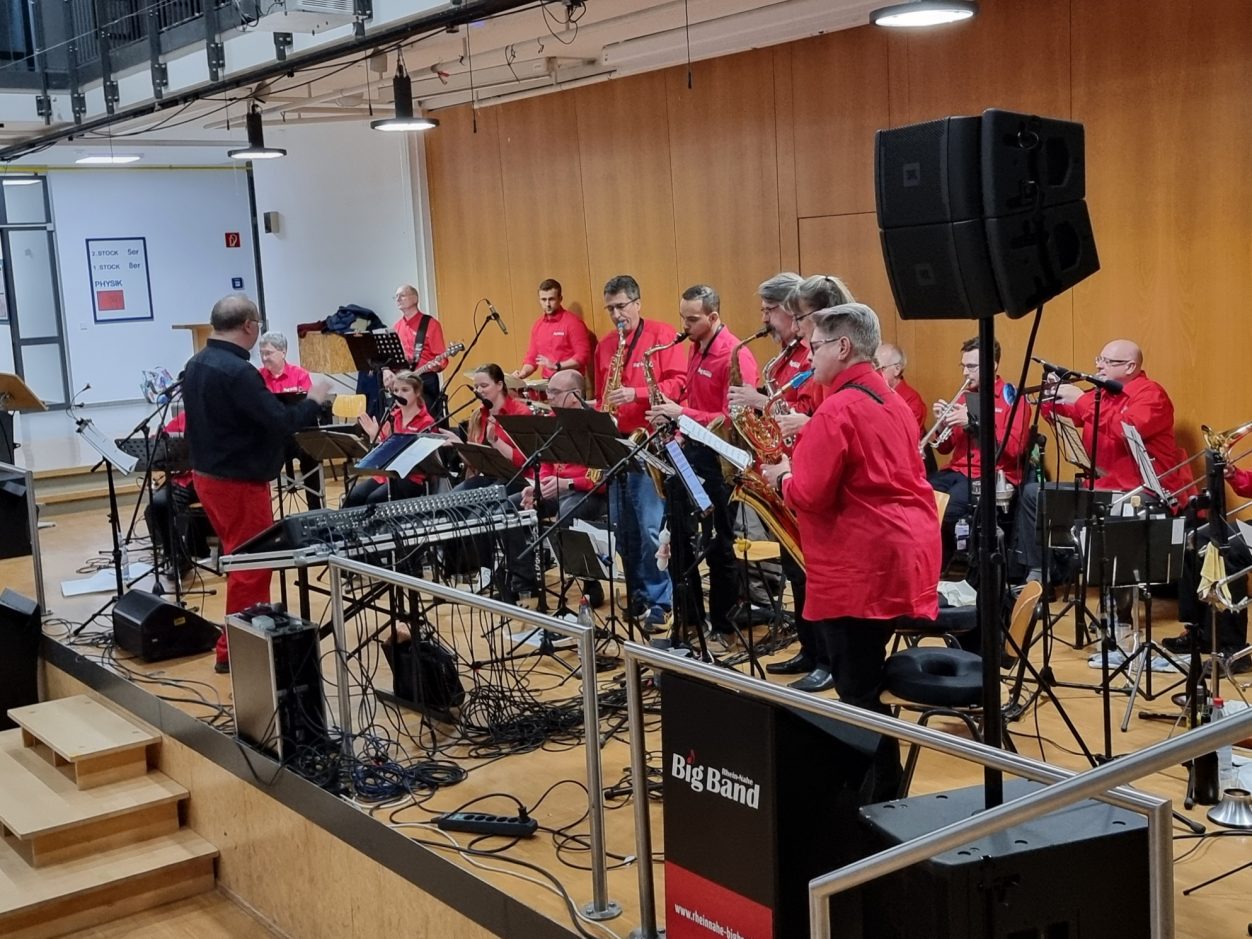 Benefizkonzert der Rhein-Nahe Big Band Eine Band mit Musikern in roten Hemden spielt in einem modernen Raum.