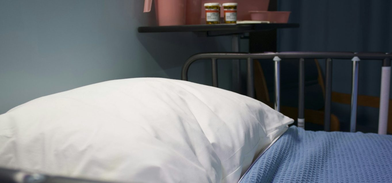 Ein leeres Krankenhausbett mit einem Kissen und einem blauen Bettlaken.