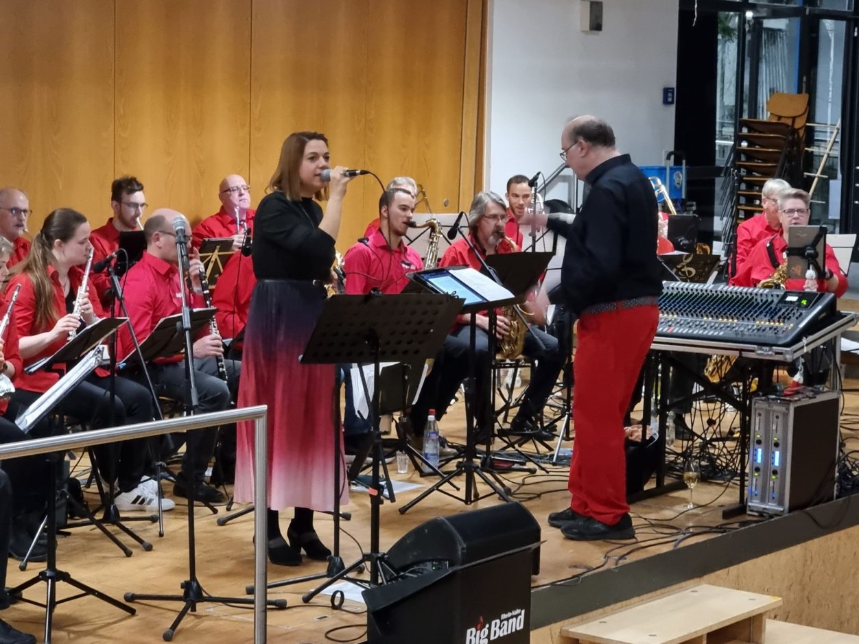 Benefizkonzert der Rhein-Nahe Big Band Eine Musikerin singt vor einer Bläsergruppe auf der Bühne.
