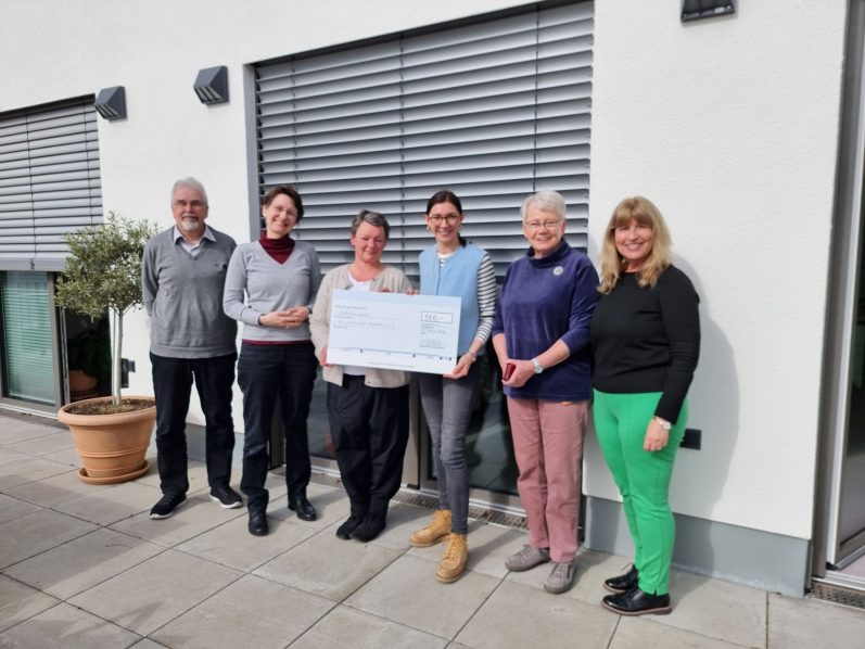 Scheckübergabe von Marie Wasem an die Hospizgruppe Ingelheim Gruppe von sechs Personen präsentiert einen großen Scheck vor einem modernen Gebäude.