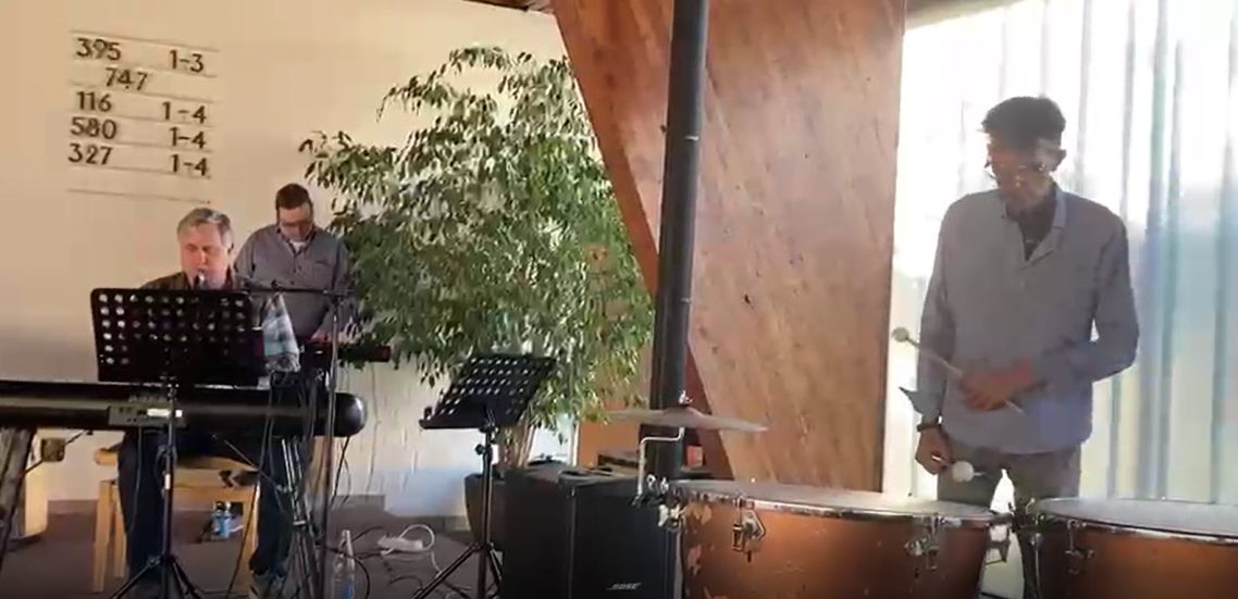 Gedenkgottesdienst am 29. April 2026 Drei Männer musizieren in einem modernen Raum mit Pflanzen und Musikinstrumenten.