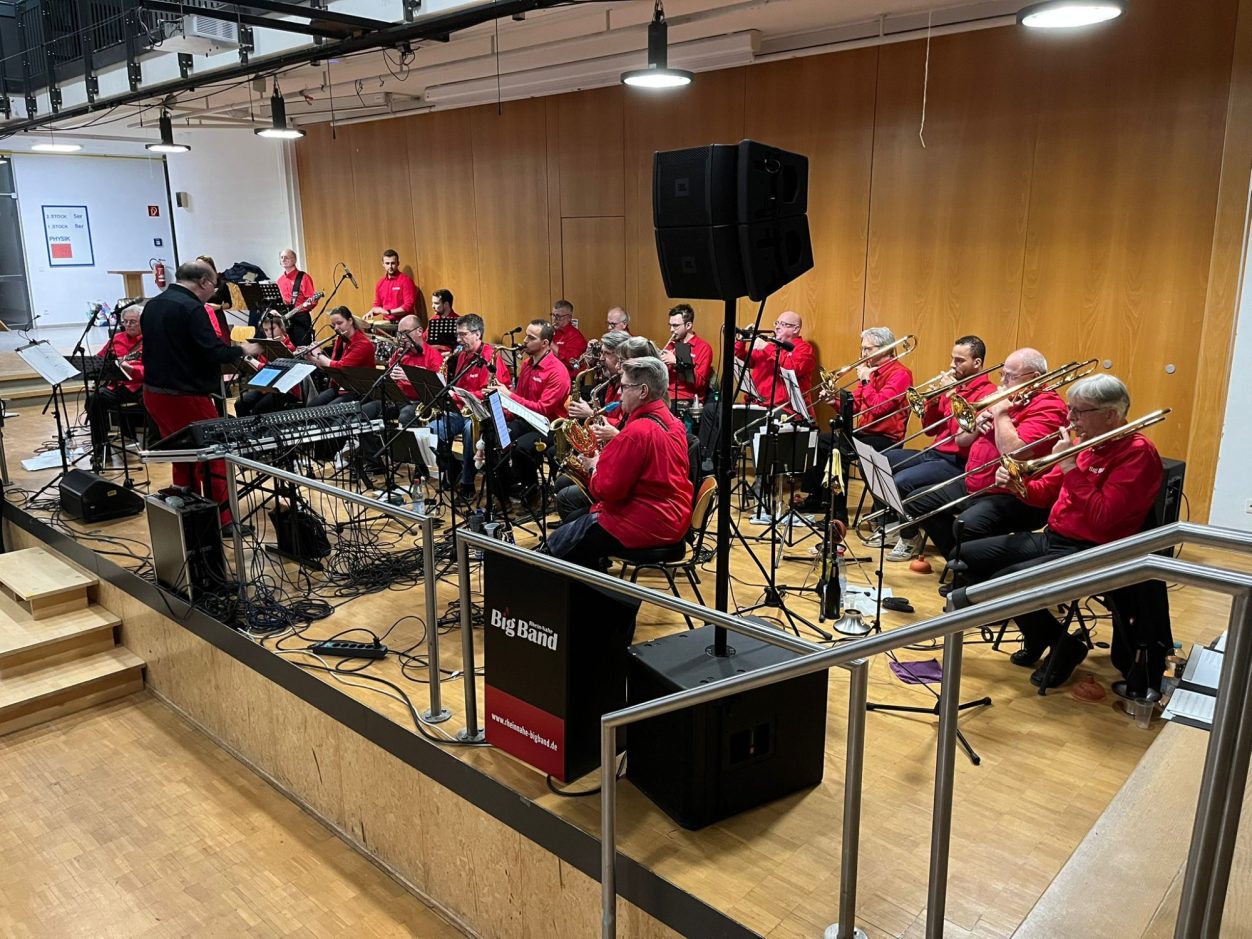 Benefizkonzert der Rhein-Nahe Big Band Die Rhein-Nahe Big Band in roten Shirts spielt auf einer Bühne in einem Innenraum.