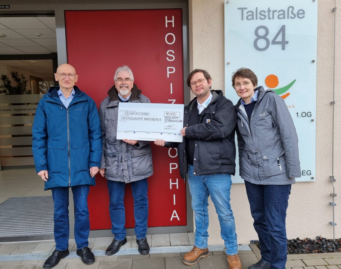 Scheckübergabe Firma Straus GmbH Vier Personen halten einen großen Scheck vor dem Eingang eines Hospizgebäudes.