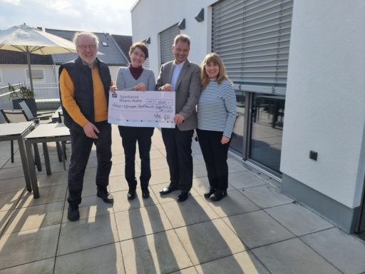 Vier Personen stehen zusammen und halten einen großen Scheck im Freien.