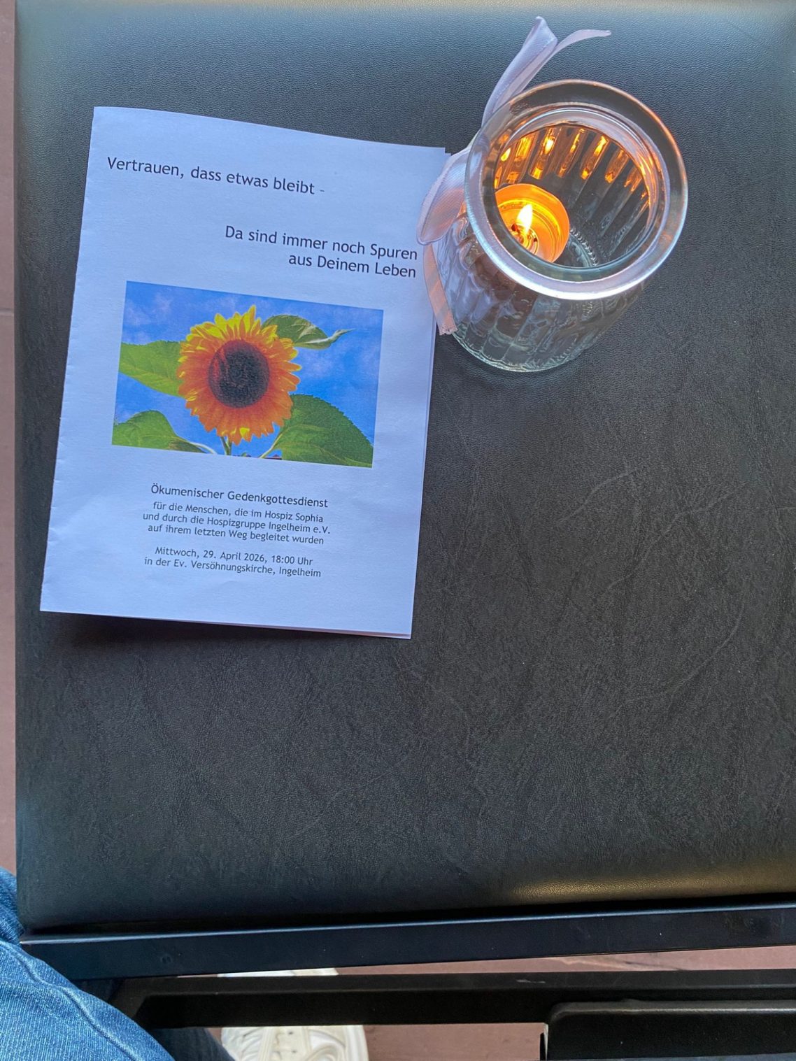 Gedenkgottesdienst am 29. April 2026 Eine Kerze in einem Glas steht neben einem Heft mit Sonnenblumenmotiv.