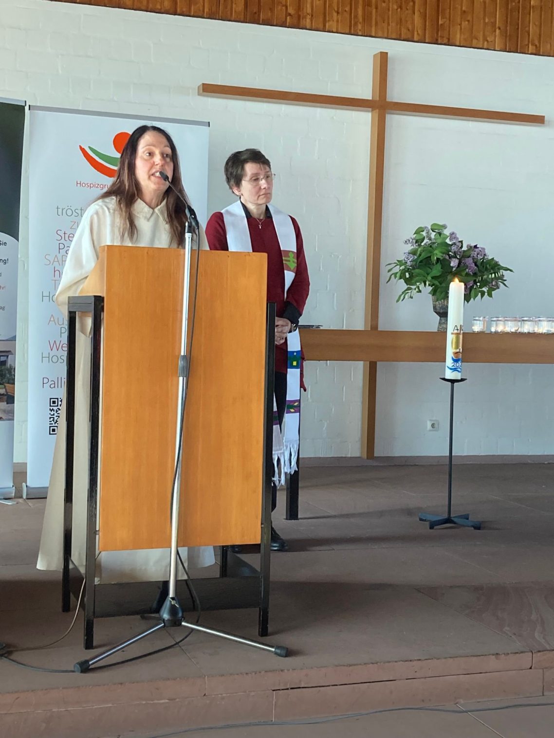 Gedenkgottesdienst am 29. April 2026 Zwei Personen stehen an einem Altar, eine predigt, eine trägt eine Stola. Im Hintergrund eine Kerze.