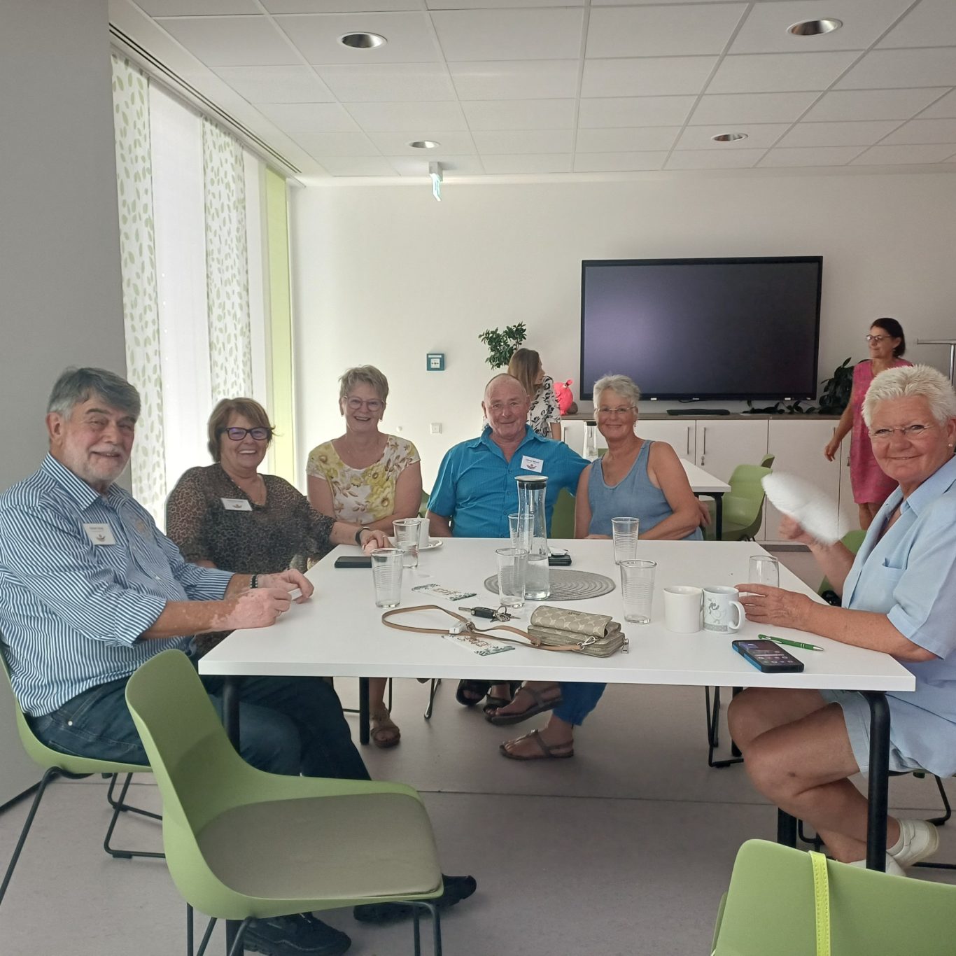 23. Juni 2026 Sommerfest für unsere ehrenamtlichen Helferinnen und Helfer Sechs Personen sitzen an einem Tisch in einem hellen Raum, freundlich miteinander kommunizierend.