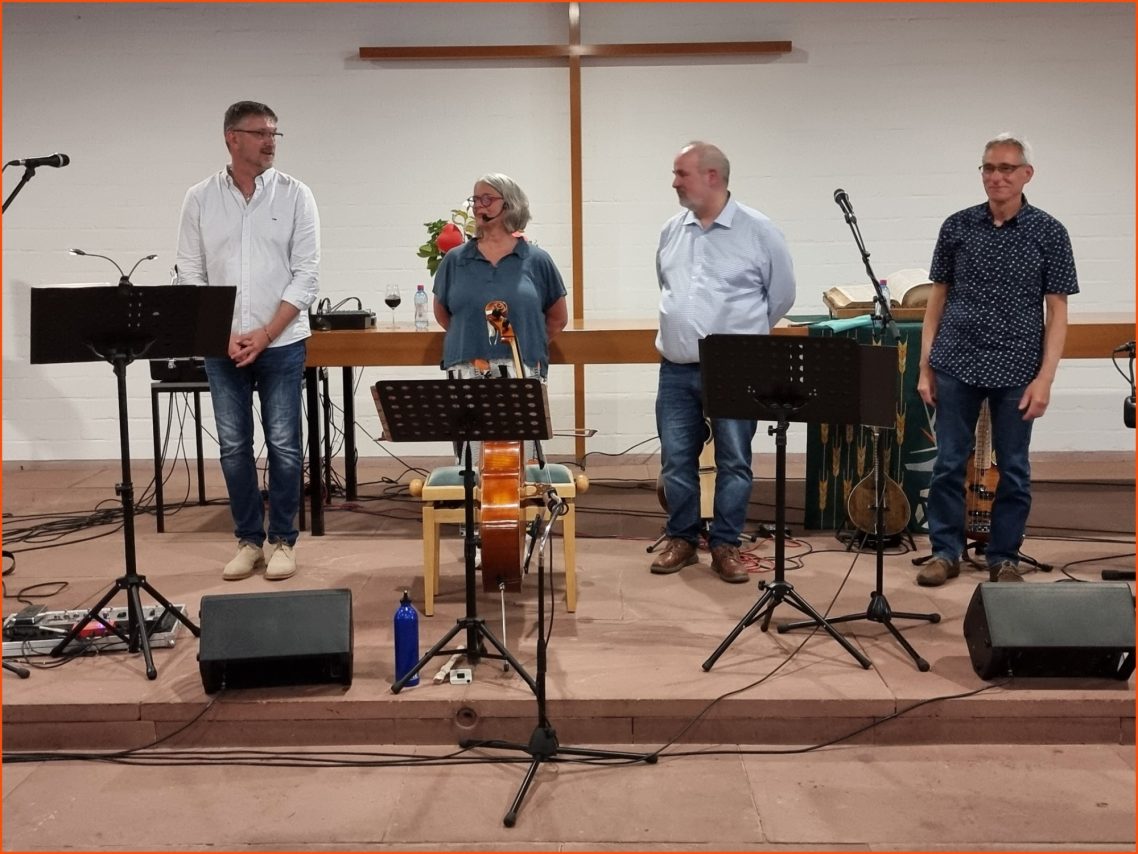 Benefizkonzert für das Hospiz Sophia - "Übers Meer - Von Meerbusen und Seesäcken" Vier Musiker stehen auf der Bühne, umgeben von Musikinstrumenten und einem Kreuz im Hintergrund.