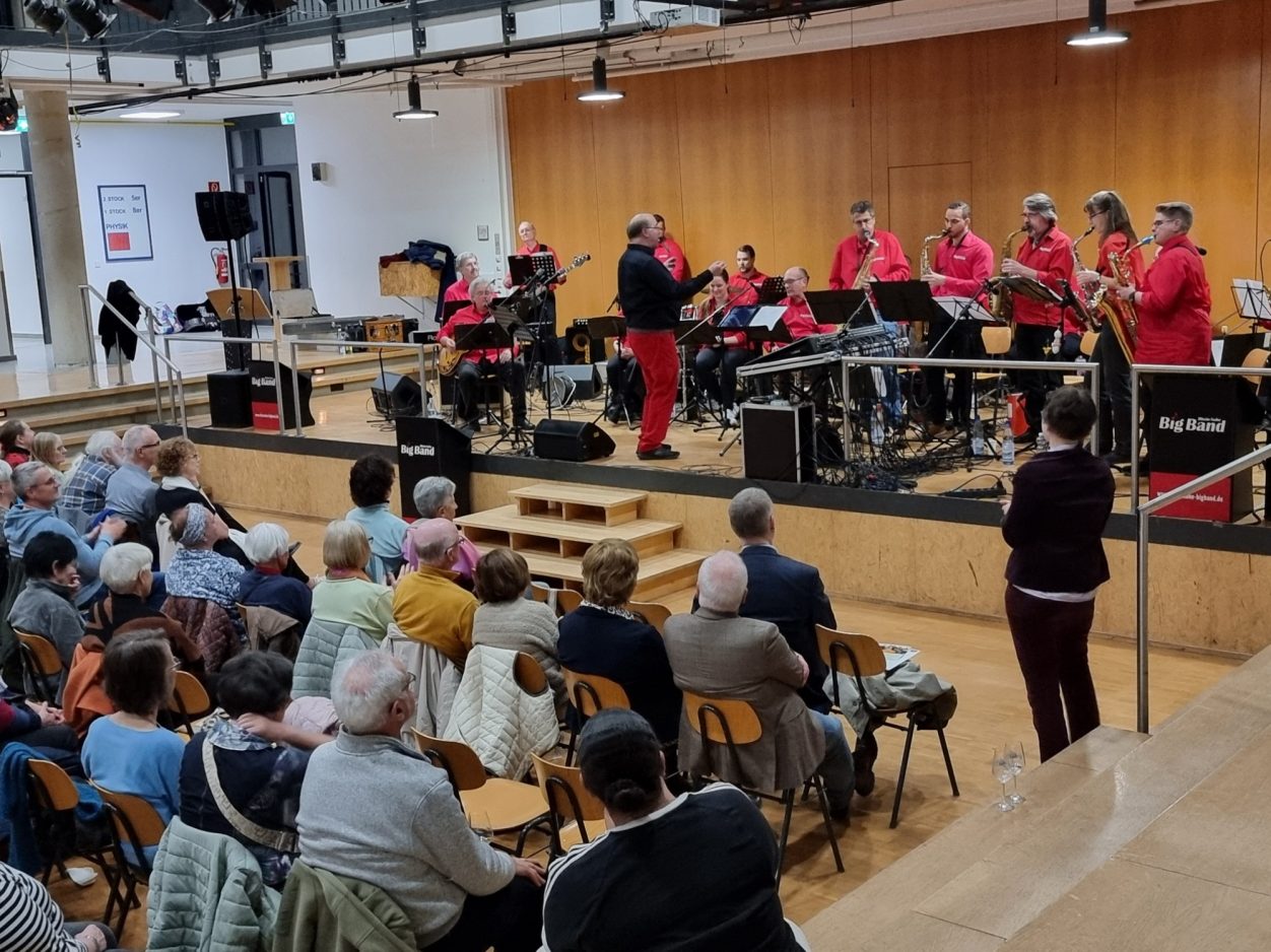 Benefizkonzert der Rhein-Nahe Big Band Die Rhein-Nahe Big Band in roten Shirts spielt auf einer Bühne in einem Innenraum.